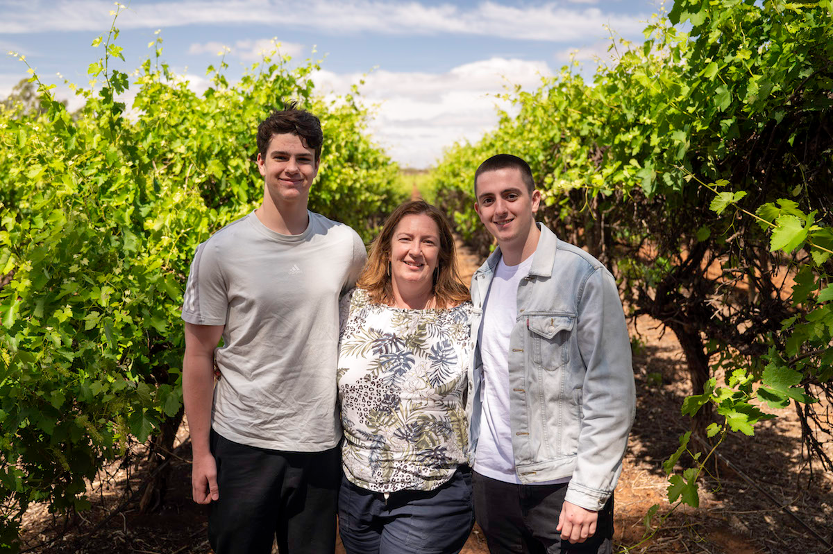 Three members of the Byrne family standing between rows of vines